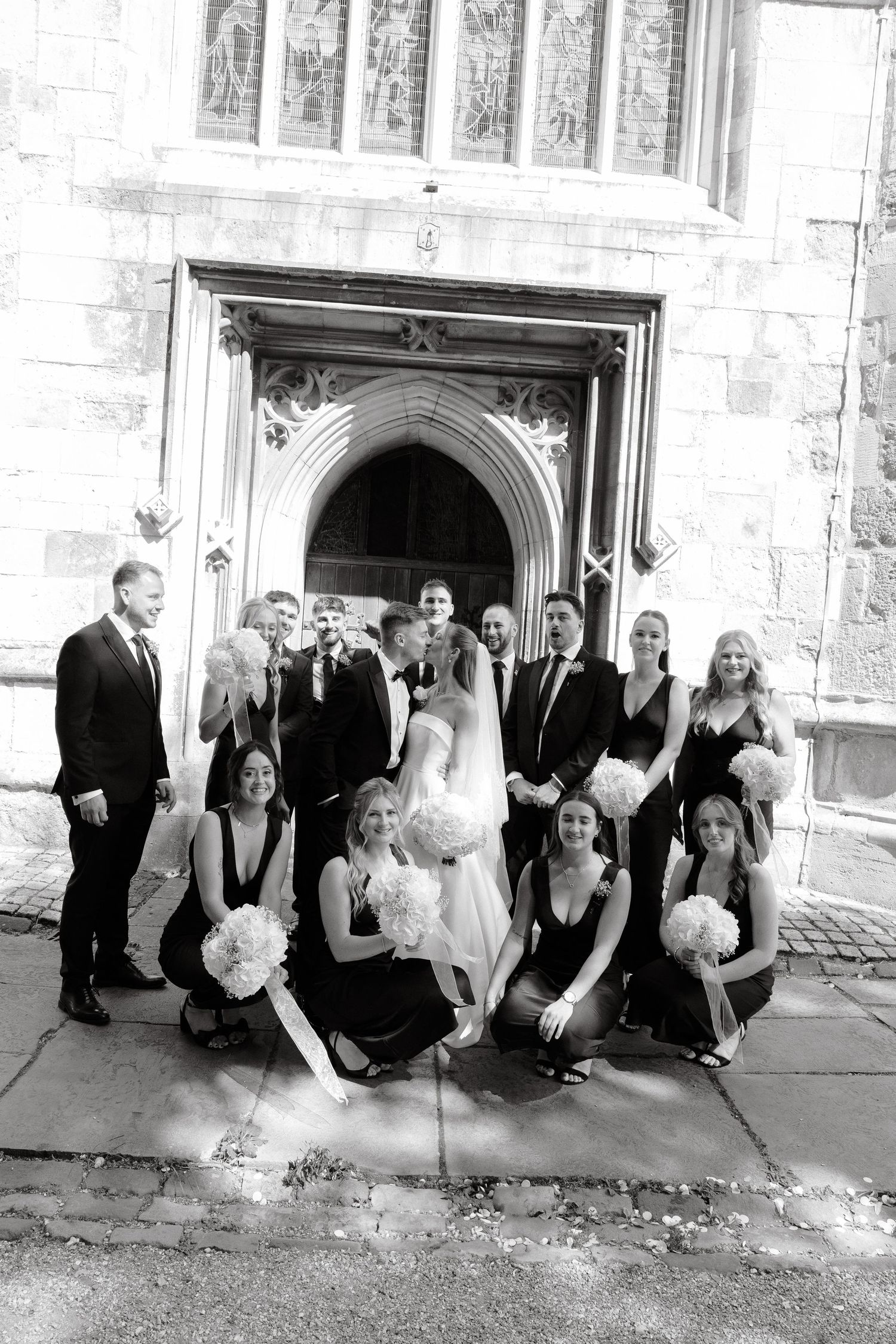 Wedding party posing together outside historic stone church entrance.