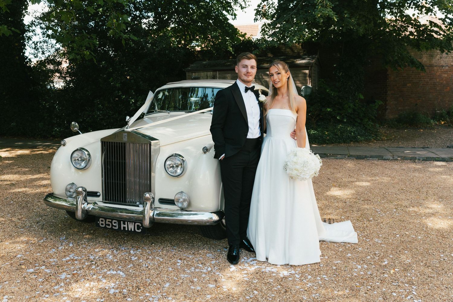A classic white Rolls Royce parked outdoors serves as an elegant wedding car.