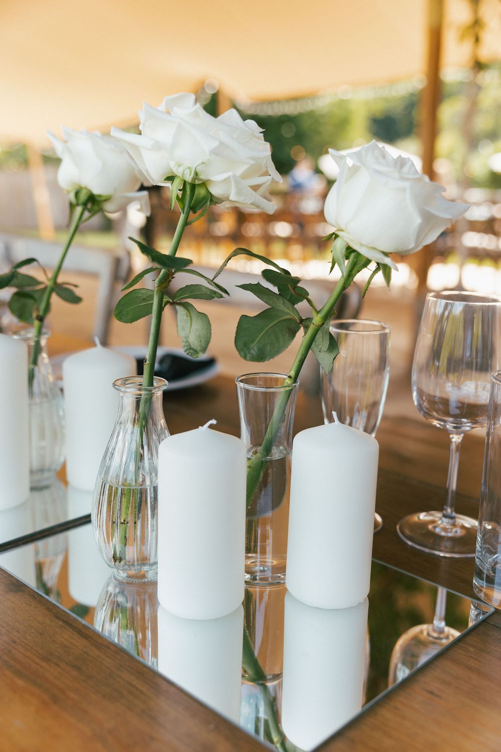 Elegant table setting with white roses in glass vases and mirror accents.