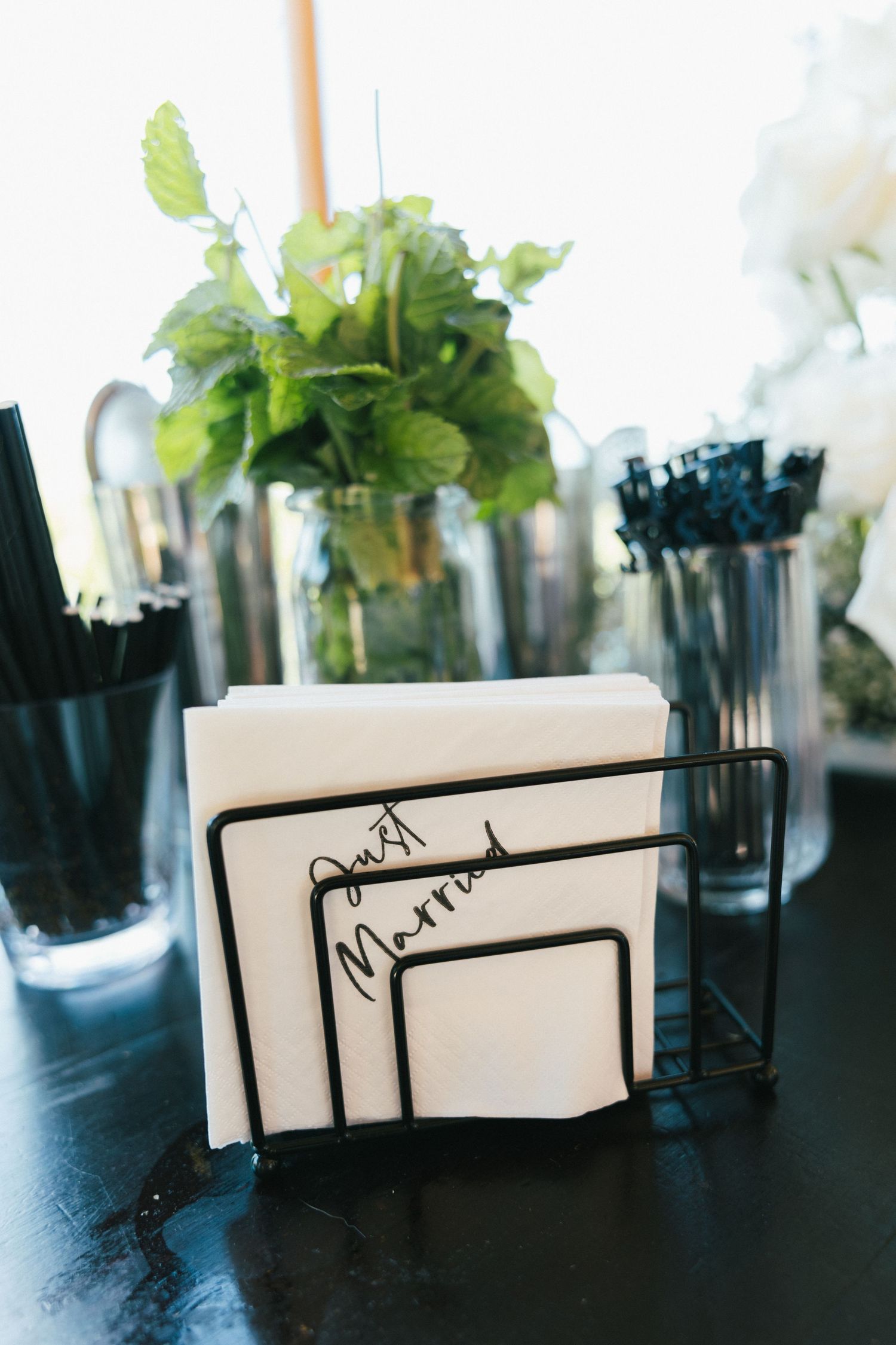 Modern place card holders and greenery arrangements on dark surface.