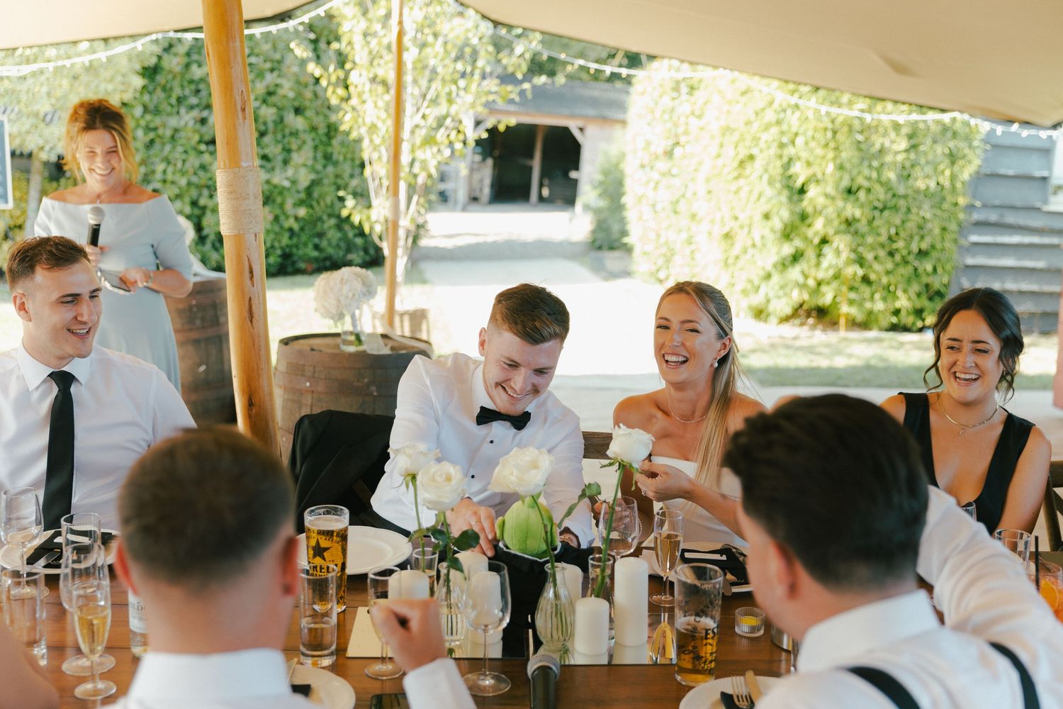 Wedding guests enjoying drinks and conversation under a covered outdoor venue.