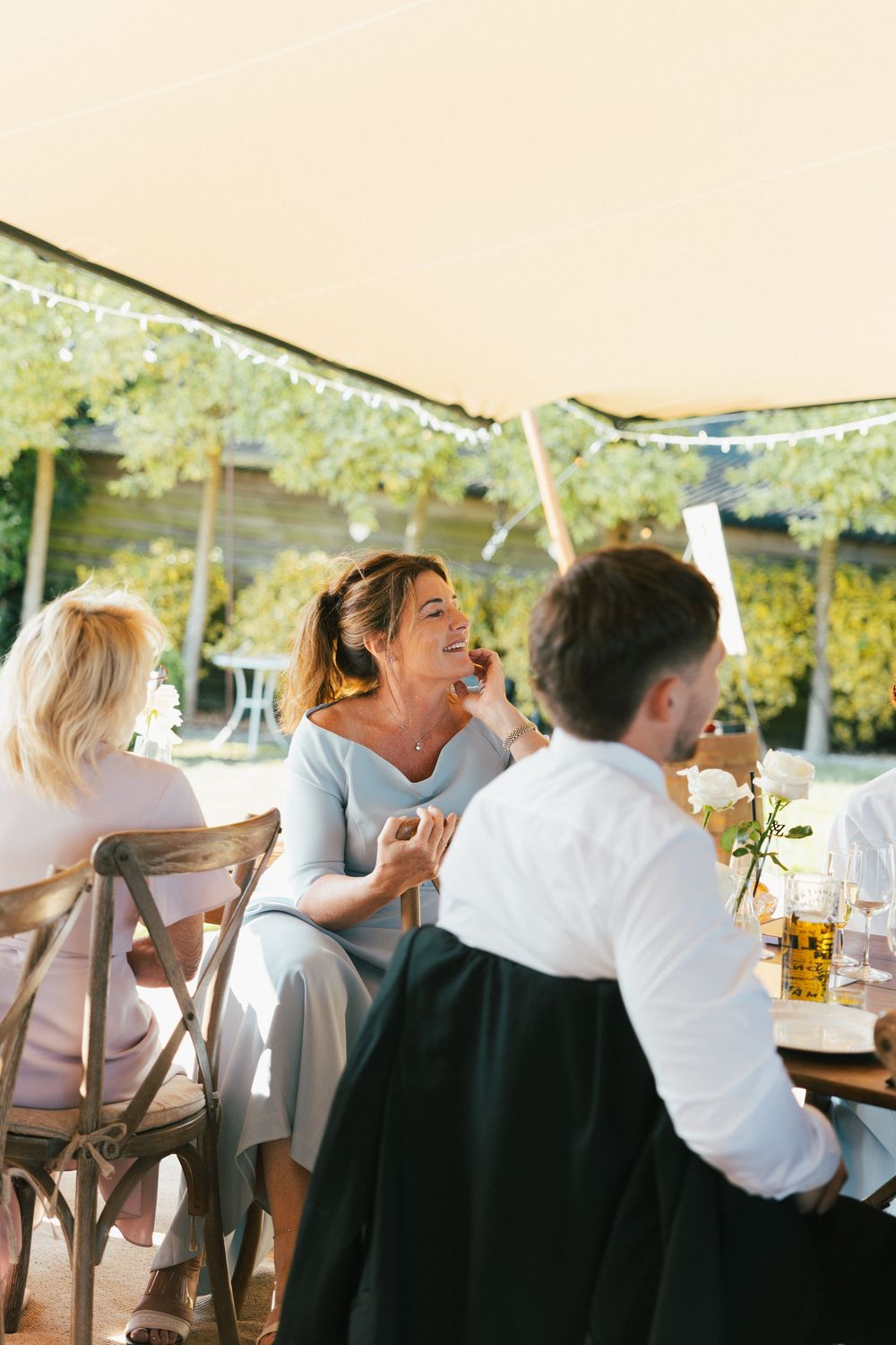 Wedding party laughing and celebrating at an outdoor reception with string lights.