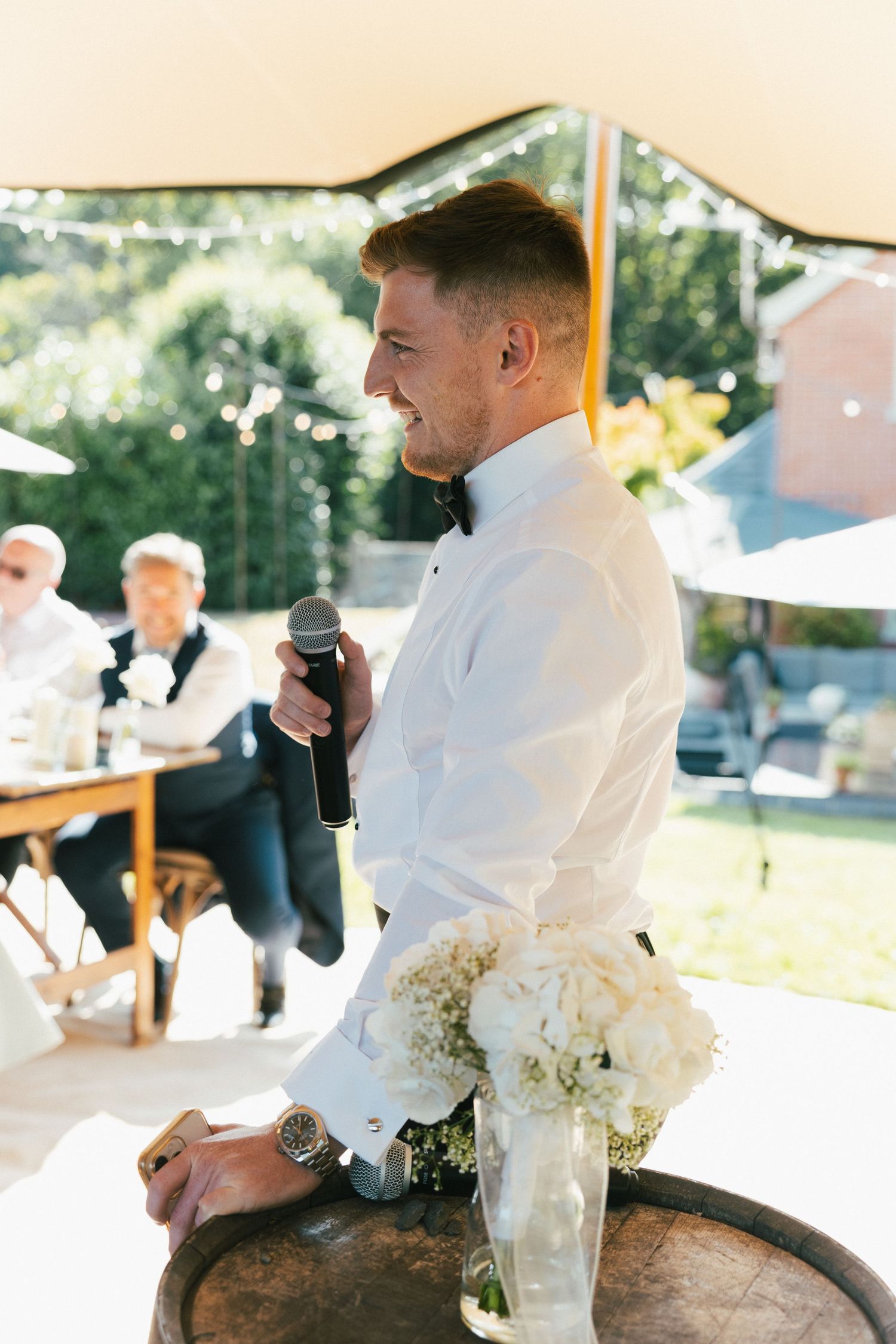 Wedding party members giving speeches at an outdoor reception near wine barrels.