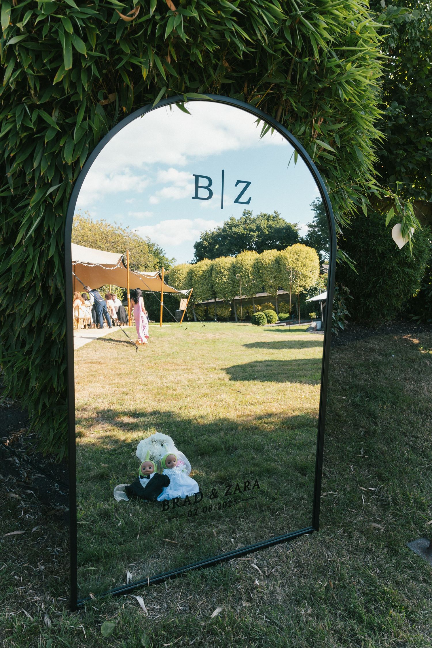 Mirror placed on grass reflects wedding scene with natural greenery backdrop.
