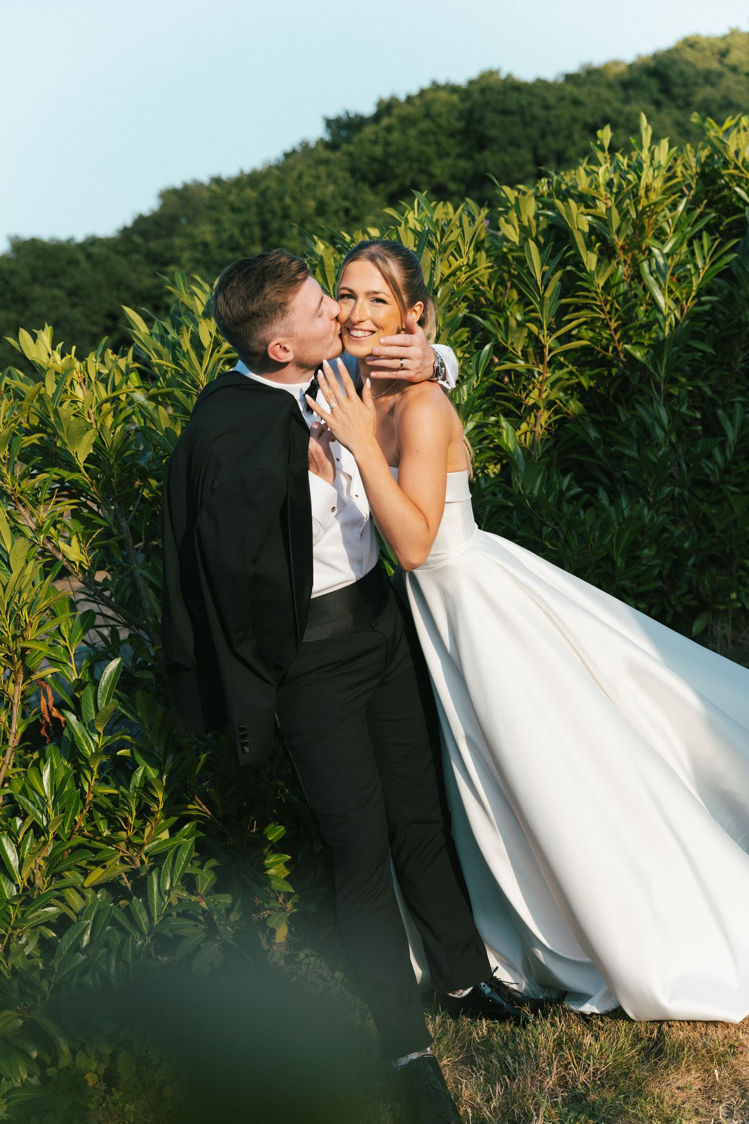 Romantic wedding couple embracing in golden sunlight among cornfield.