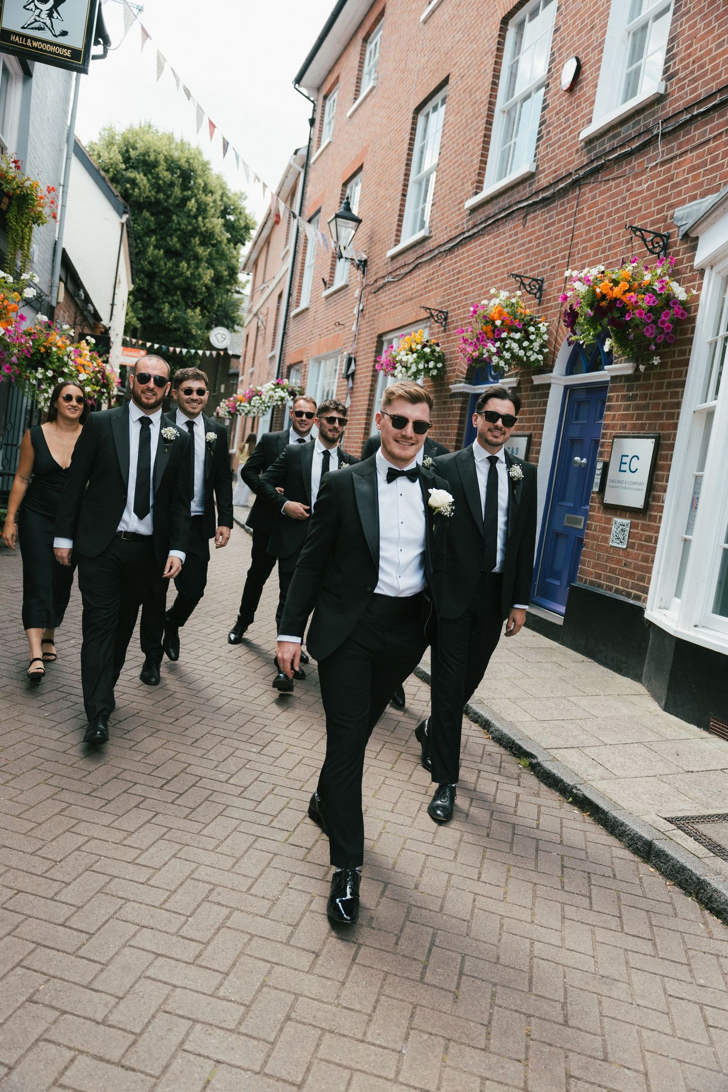Wedding party walking down a brick-paved street wearing formal black attire.