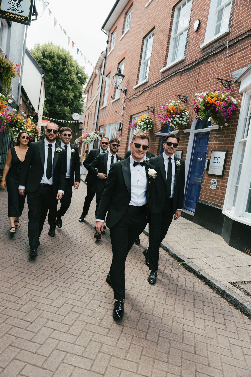 Wedding party walking down a brick-paved street wearing formal black attire.