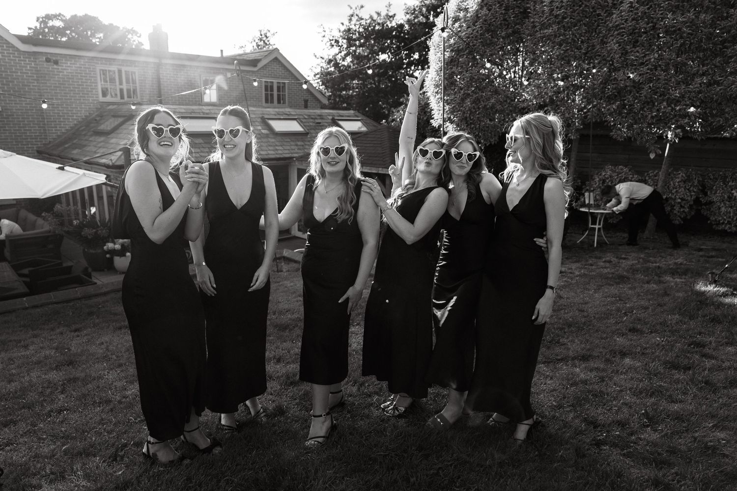 A group in black dresses poses outdoors at a formal event in sequence.