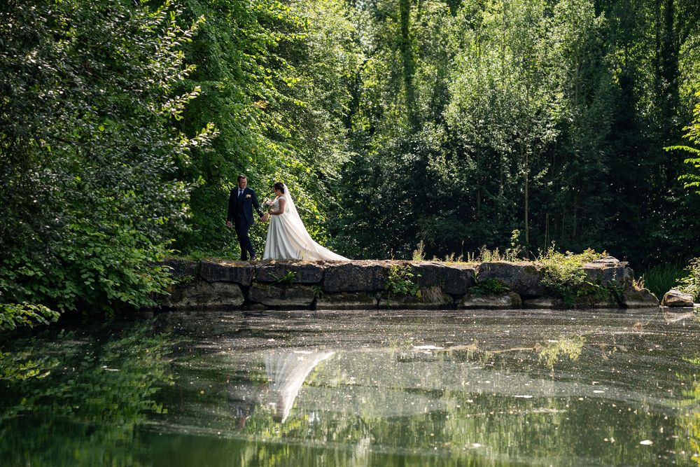 A scenic outdoor wedding ceremony setup in a lush forest with wooden chairs and floral arrangements along the aisle.