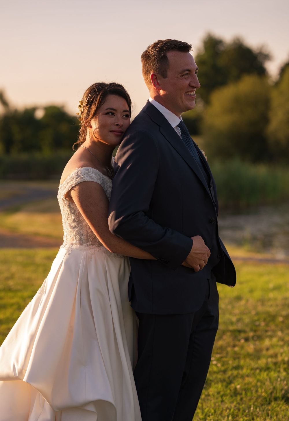 A couple in wedding attire shares an intimate moment at sunset in a grassy field.