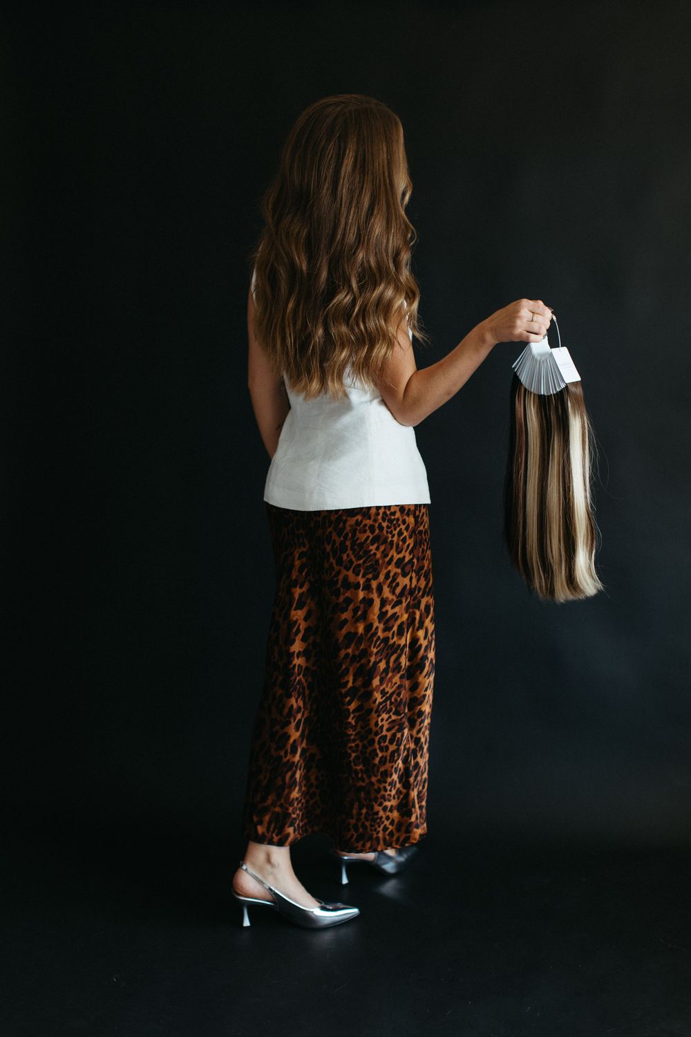 Woman in leopard print midi skirt and white sneakers poses against dark background in fashion photoshoot series.