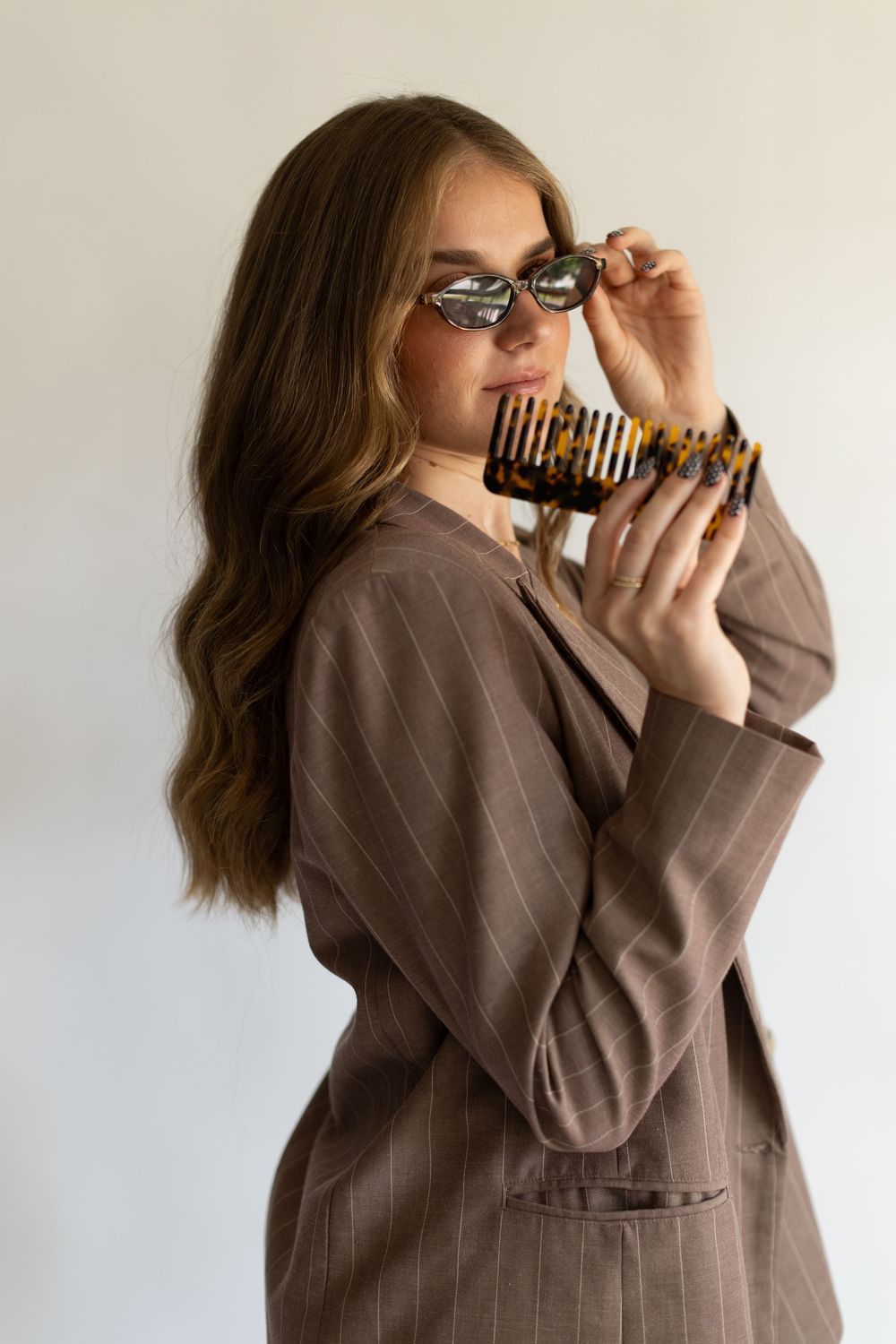 Person in brown pinstriped blazer drinking from a striped coffee cup.