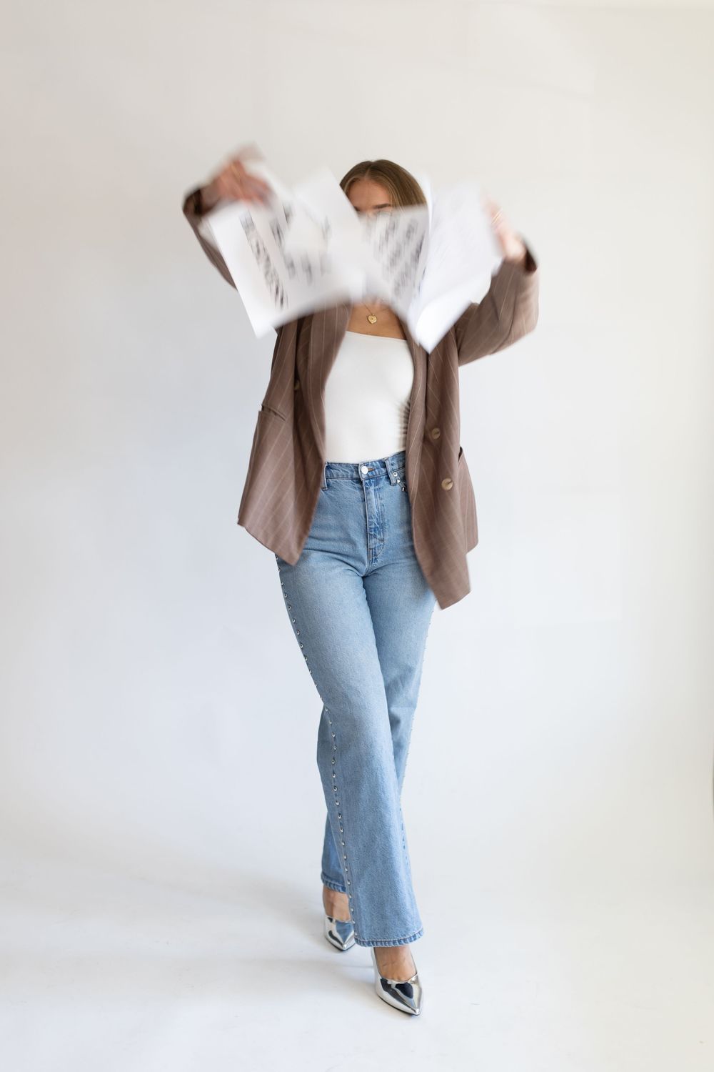 Fashion shot showing brown blazer, white top and light blue jeans with silver heels against white background.