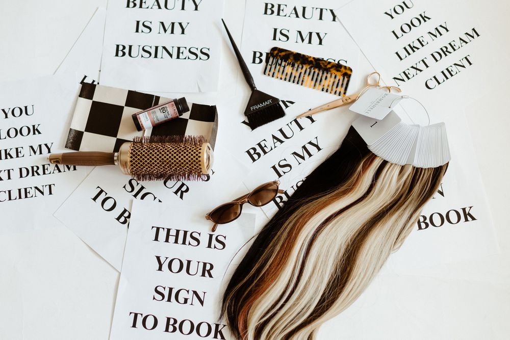 Flatlay of beauty and business related text snippets with makeup brushes and hair accessories on white background.