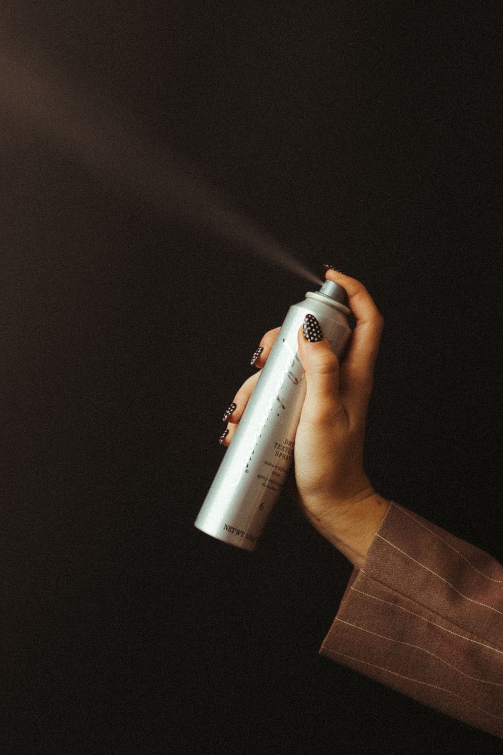 Hand holding a silver aerosol spray can against a dark background.