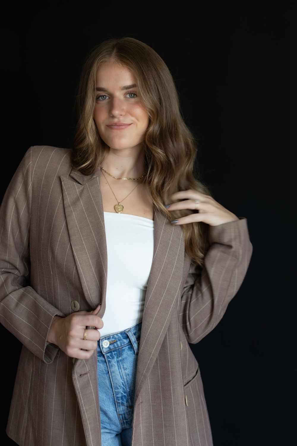 A person wearing a brown pinstripe blazer and white top poses against a dark background in a fashion photoshoot series.