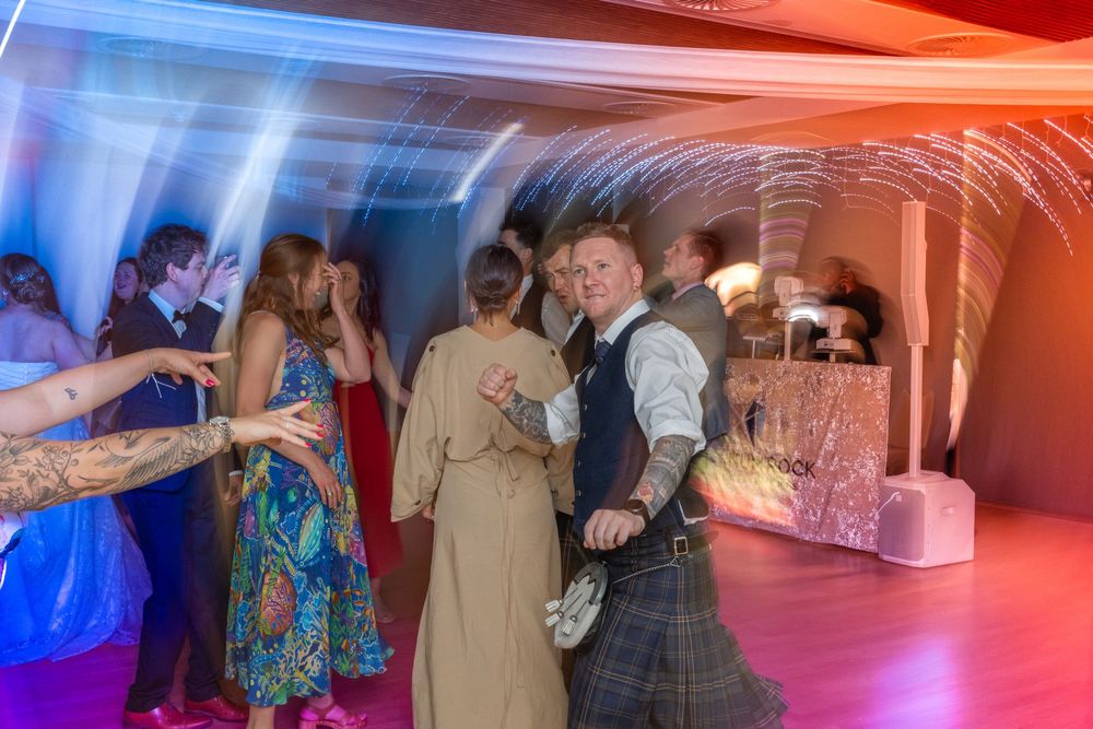 People dancing and socializing at a wedding reception with colorful mood lighting in an elegant venue.