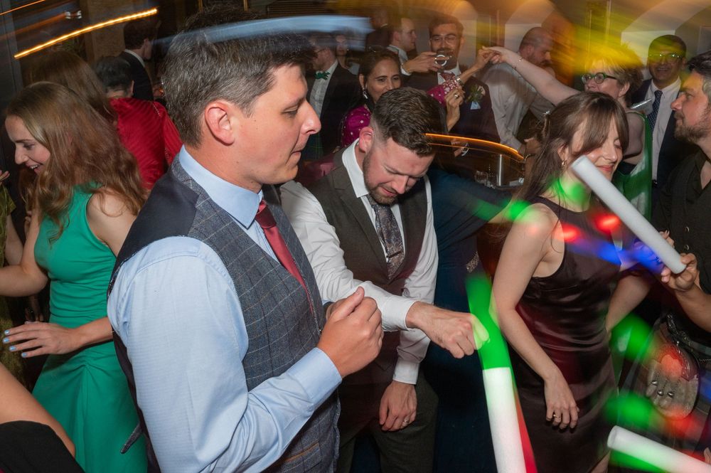 People dancing and socializing at a crowded party with green lighting effects in the background.