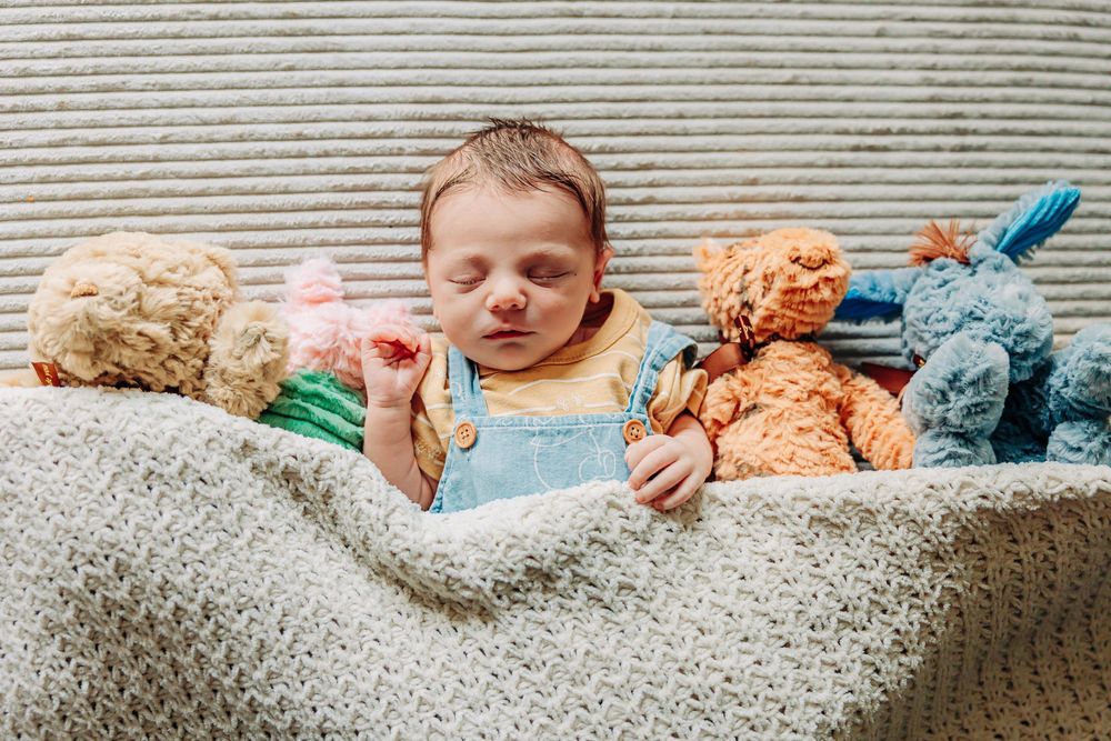 A sleeping baby rests peacefully on a textured gray couch with toys scattered nearby.