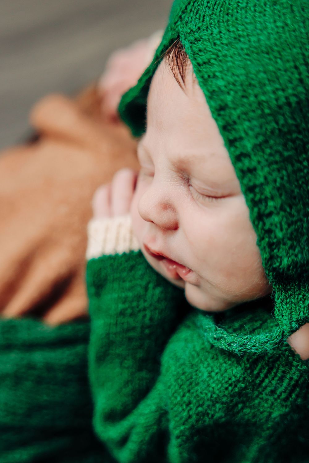 Sleeping baby wrapped in bright green knit blanket shown in close-up profile.