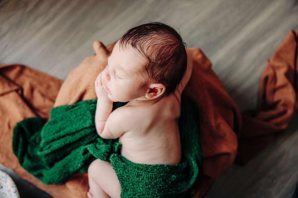 A newborn baby wrapped in green and brown blankets lies peacefully during a photography session.