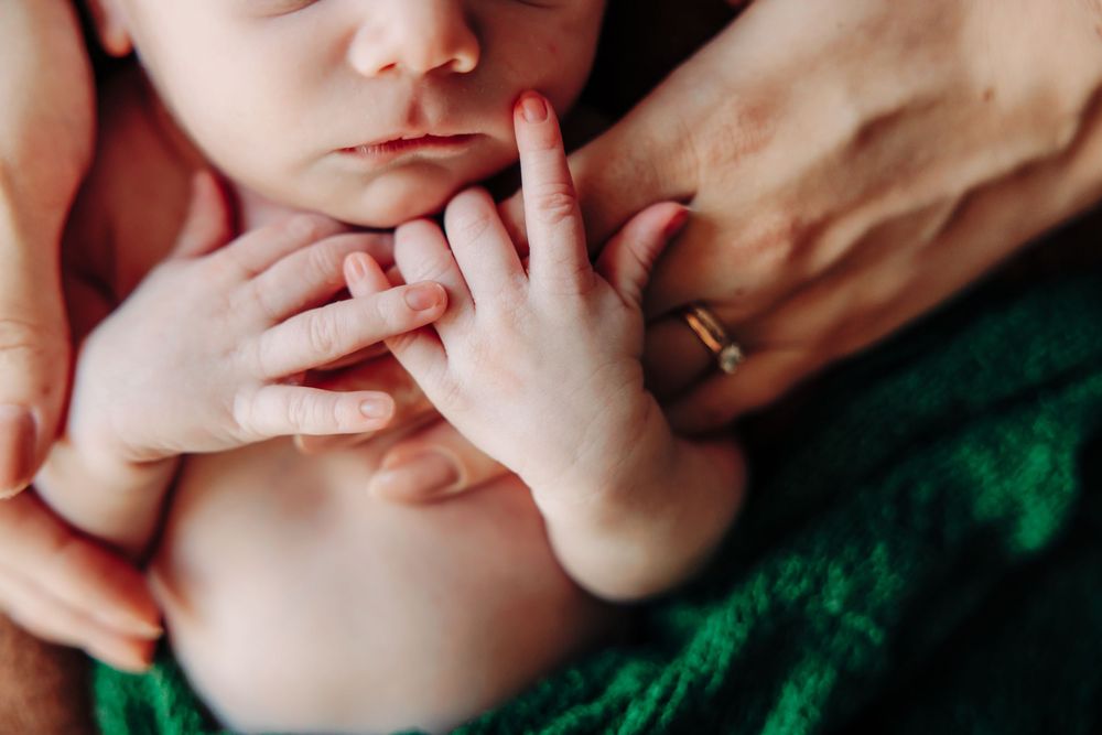 Gentle hands touching sleeping baby's face wrapped in green knit fabric.