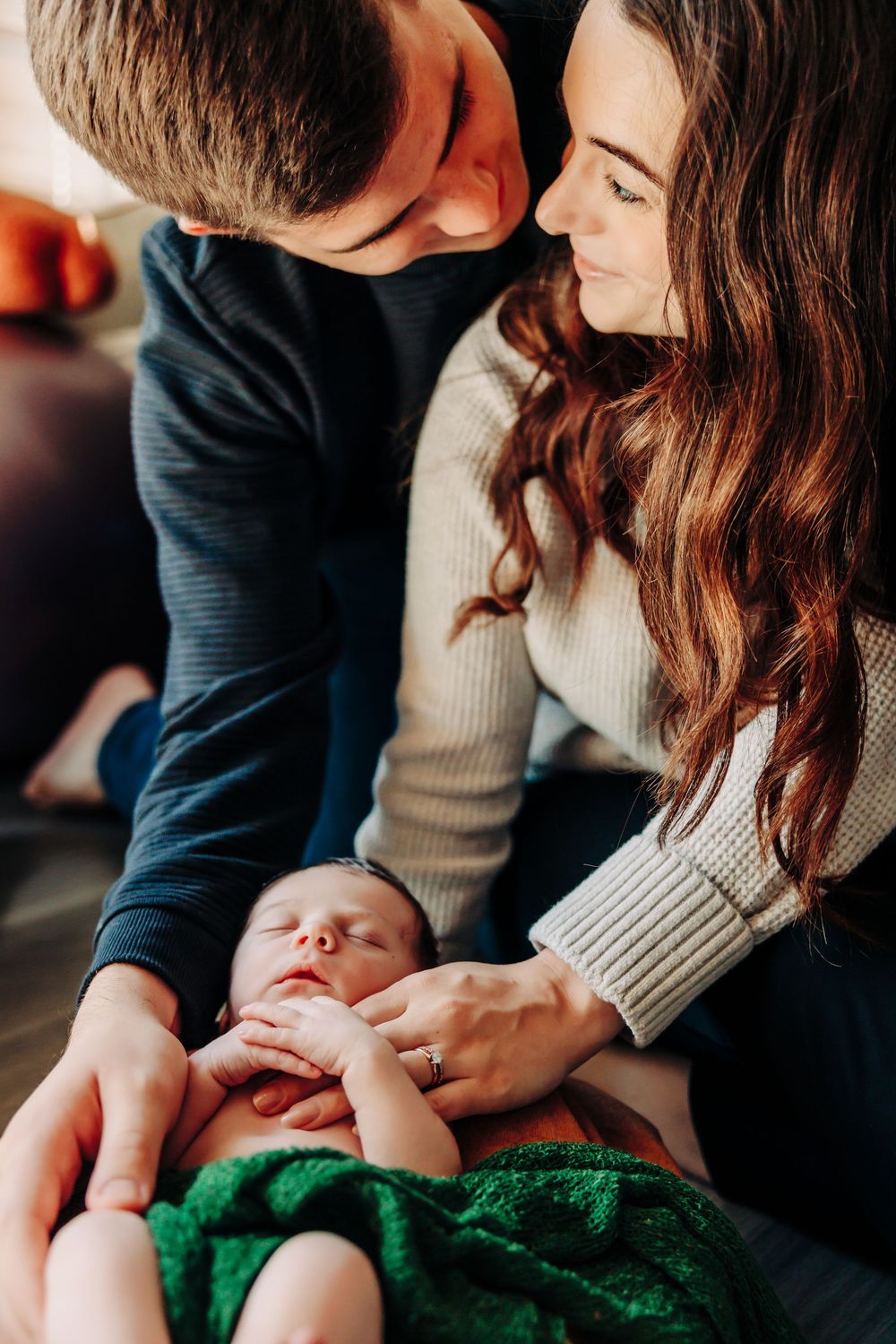 Intimate family moment as parents lovingly attend to their newborn wrapped in green on wooden flooring.