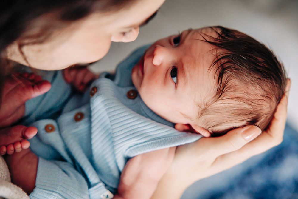 Newborn baby sleeping peacefully in a soft blue onesie while being held in gentle arms.