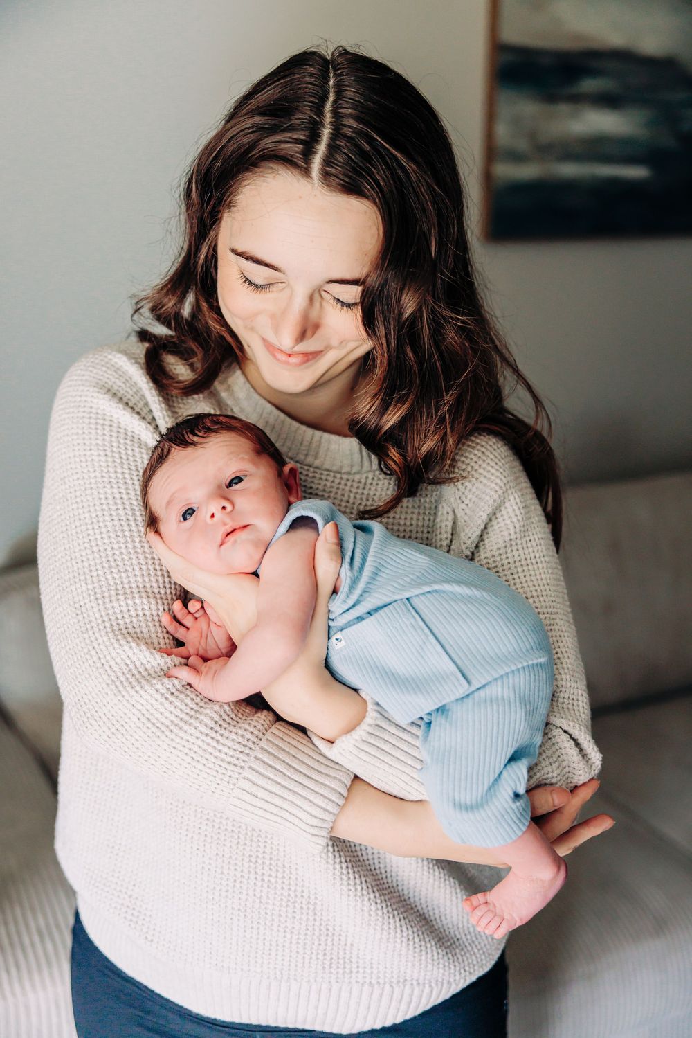 A parent in a cream sweater cradles and bonds with their sleeping newborn baby in soft natural light.