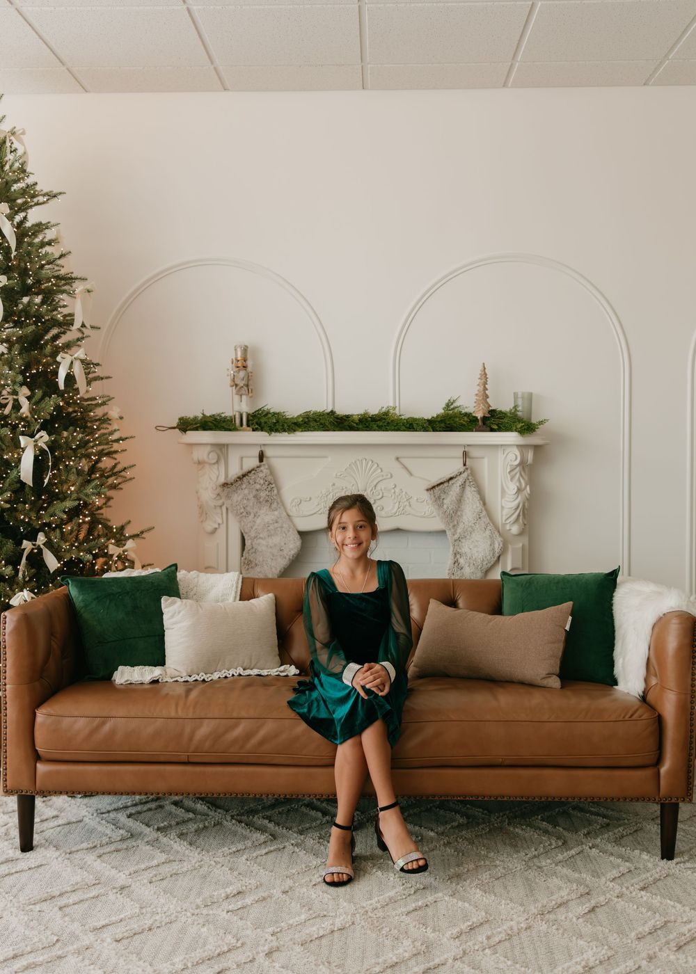Modern holiday living room with brown leather couch, Christmas tree, and white marble fireplace with stockings.