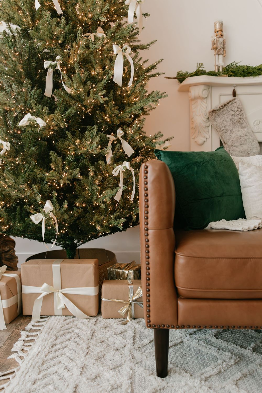 A decorated Christmas tree stands beside a brown leather armchair on a light gray patterned area rug.