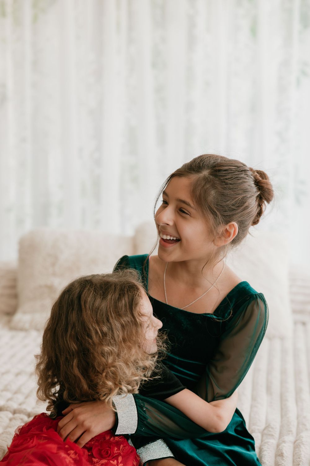 A mother and daughter share a joyful moment together while wearing elegant holiday dresses in green and red.