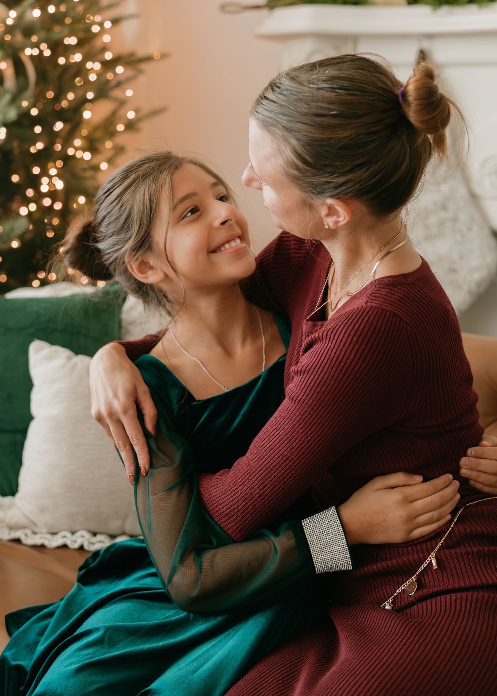 A tender moment shared between two people wearing burgundy and green sweaters in front of a Christmas tree.