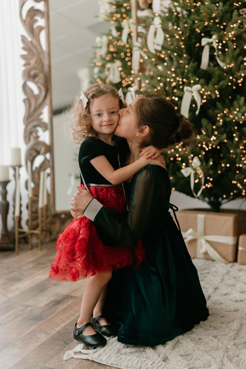 Sweet holiday moment shared between two people in formal attire by a decorated Christmas tree with twinkling lights.