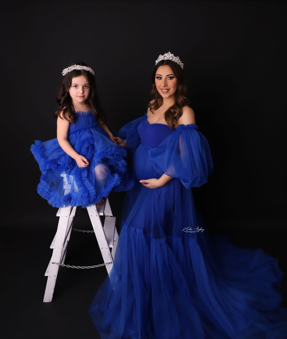 A maternity portrait with a child on a white ladder, both wearing royal blue dresses.