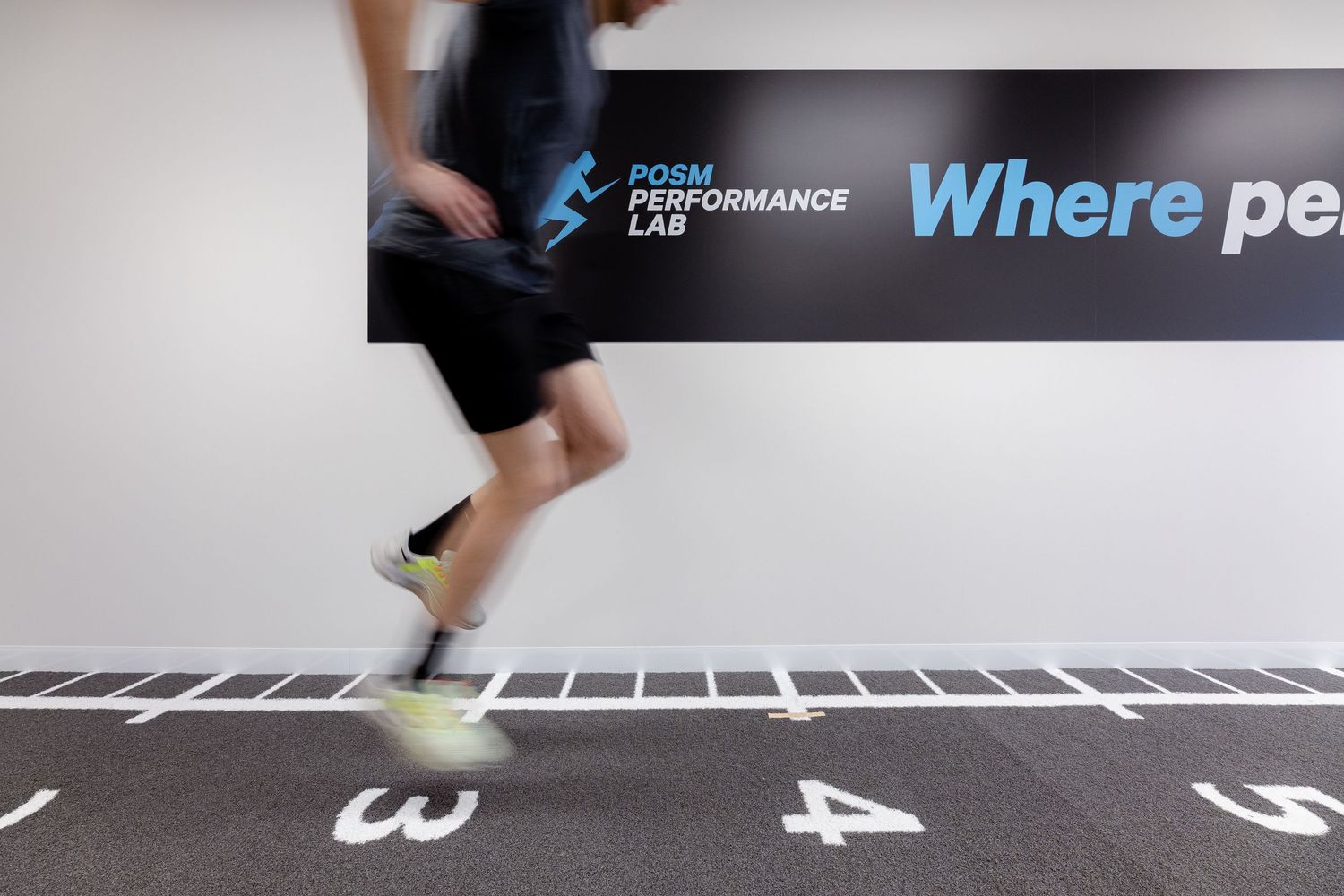 Runners in motion on a marked track with painted white lines and numbers during a race or training session.