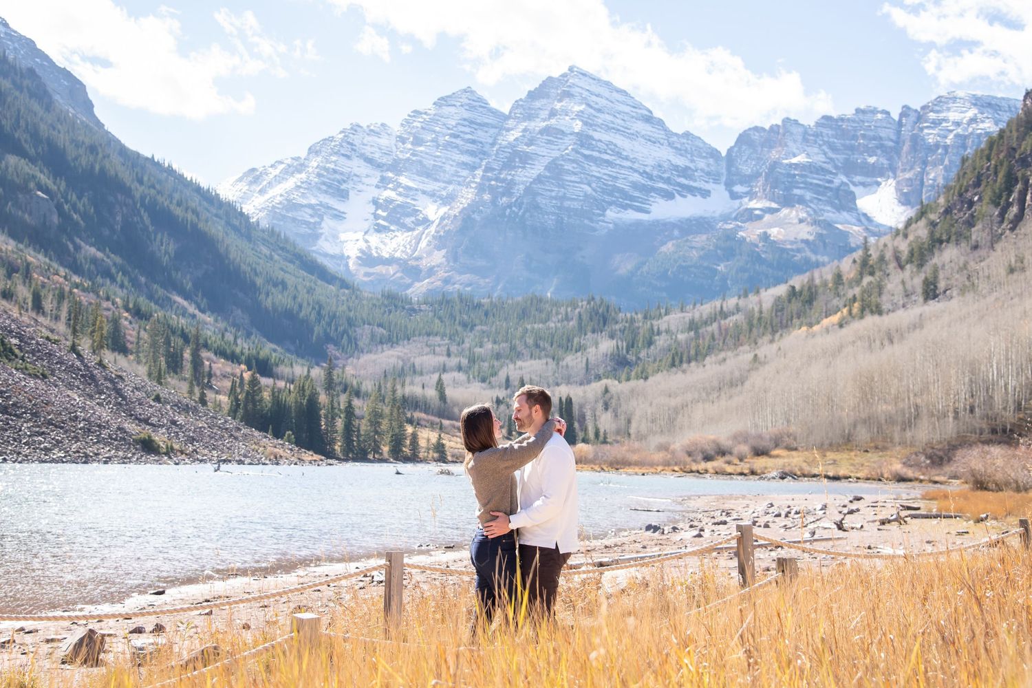 Panoramic mountain landscape with couple and snow-capped peaks and golden meadow in the foreground at Maroon Bells, Colorado.