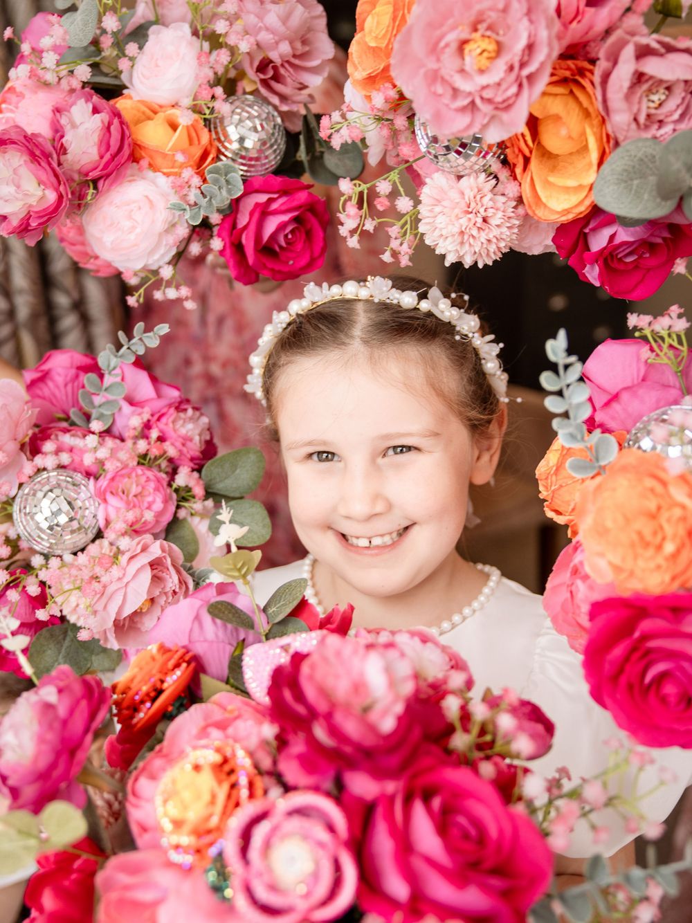 A floral portrait surrounded by vibrant pink, orange and coral roses with pearl and crystal decorative elements.