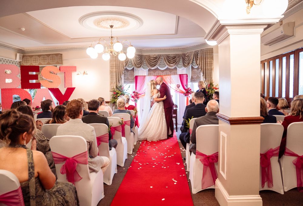 Wedding reception venue decorated in elegant red and white with chandeliers and chair covers.