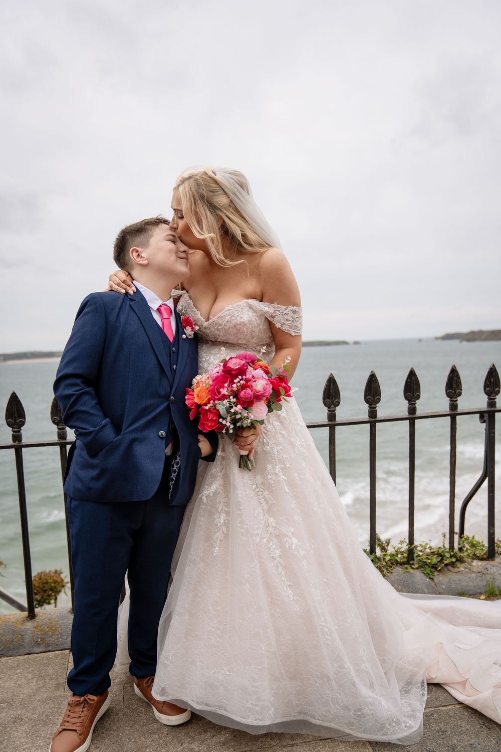 A romantic wedding couple shares intimate moments by the ocean with a black iron railing in the background.