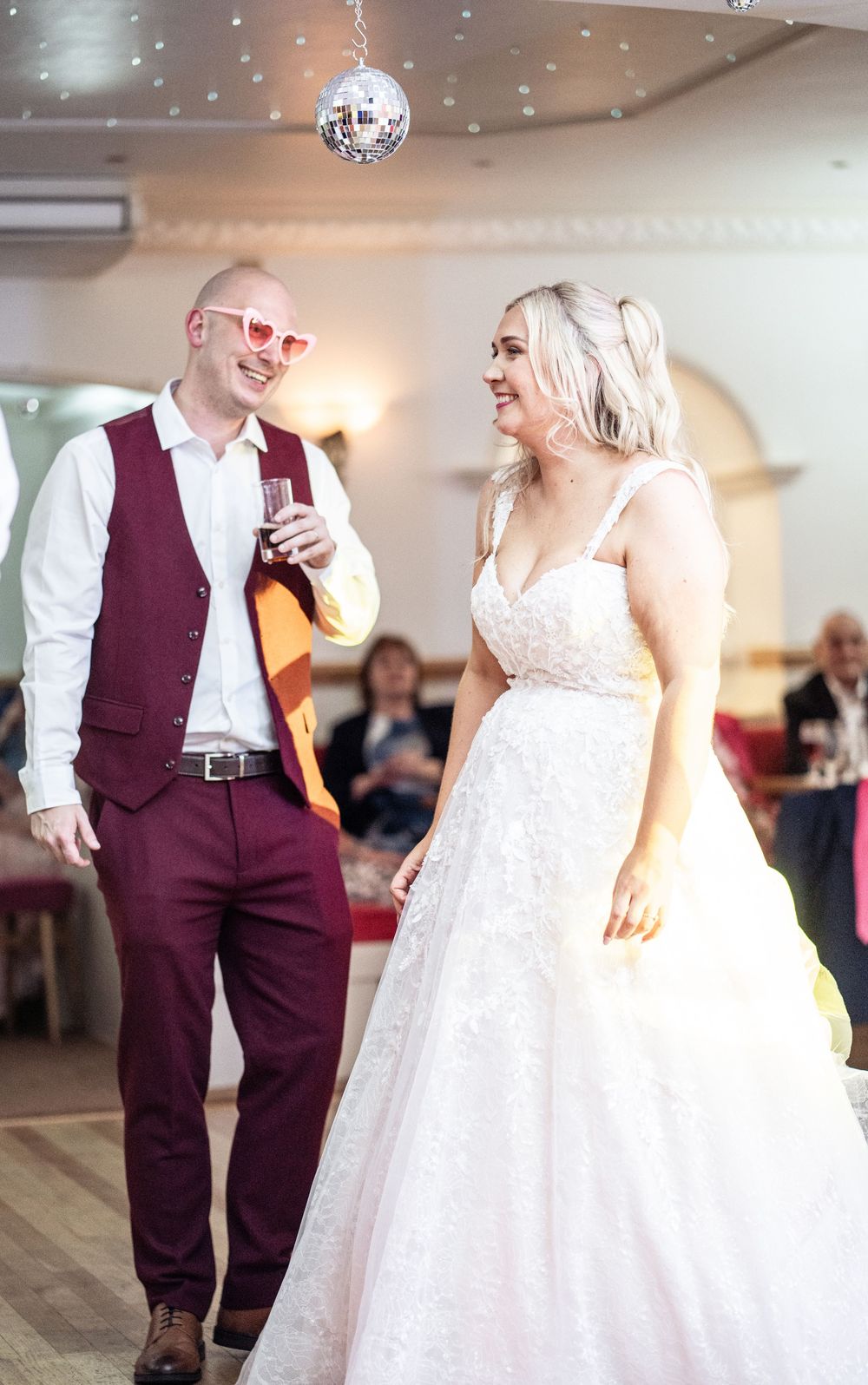 A couple dances together at a wedding reception under disco ball lighting.