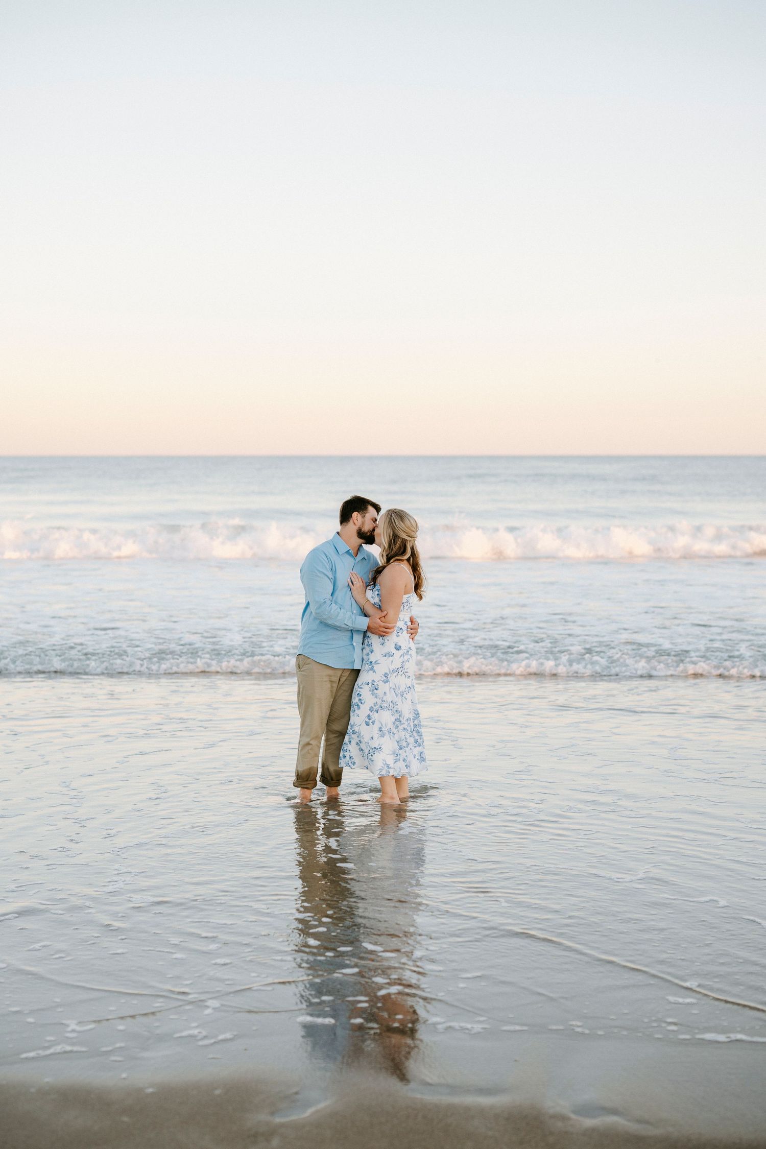 A couple shares a romantic moment while standing in shallow ocean waters at sunset on a peaceful beach.