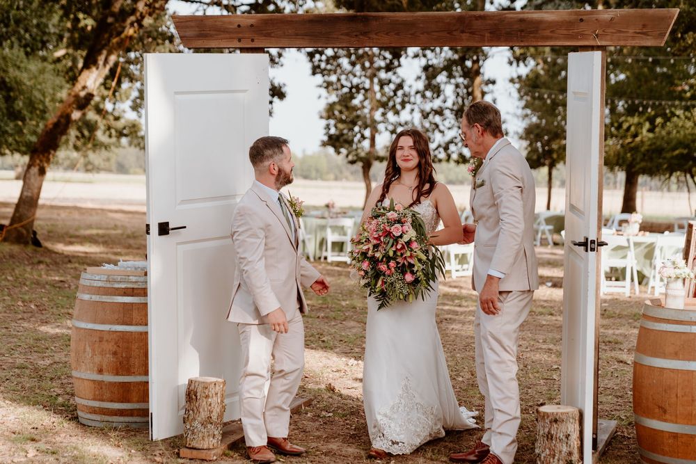 Bride and groom standing at rustic outdoor wedding altar with white doors and wooden wine barrels.