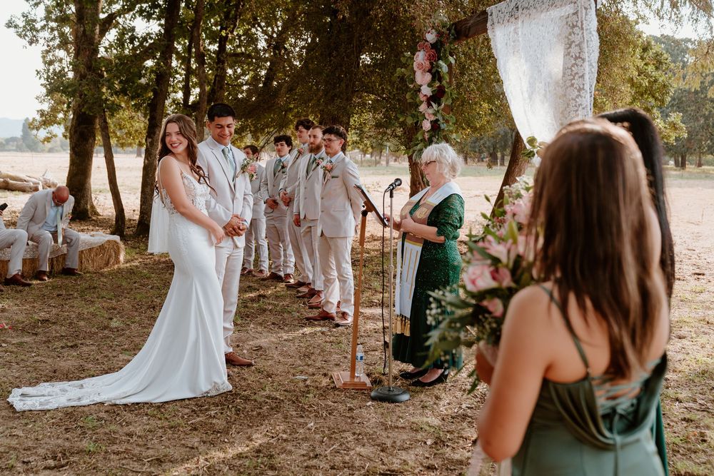 Bride and groom holding hands at outdoor wedding ceremony altar surrounded by groomsmen and bridesmaids.