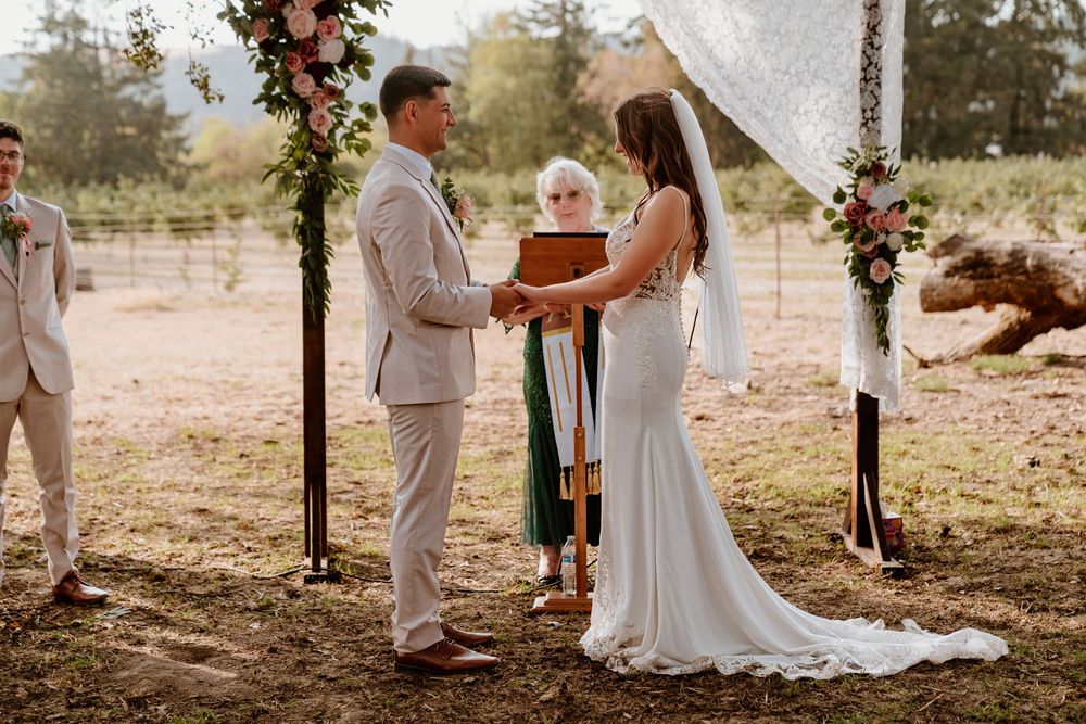 Couple exchanges vows at rustic outdoor wedding altar adorned with pink and white floral arrangements.