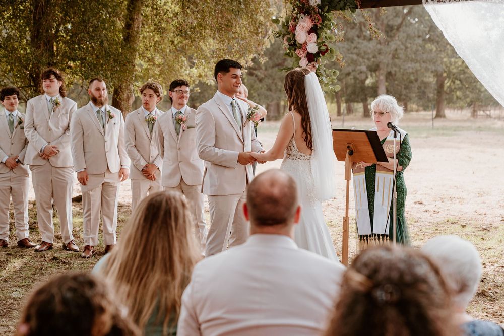 Groom and bride share vows as groomsmen in tan suits stand beside them at outdoor ceremony.