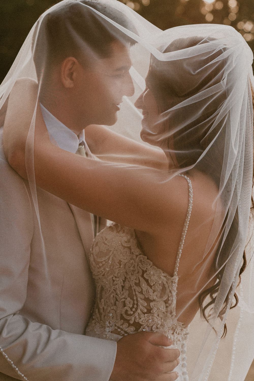 Bride and groom share intimate moment together draped under a flowing wedding veil.