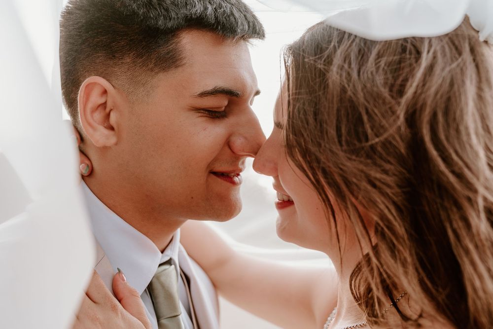 Bride and groom share an intimate nose-to-nose moment, smiling softly on their wedding day.