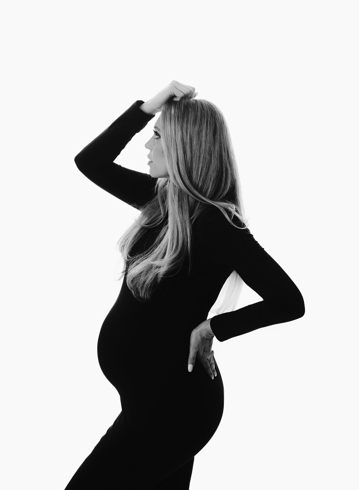 Black and white maternity portrait on a white background. Expectant mom in a fitted black dress at our North Austin photography studio.