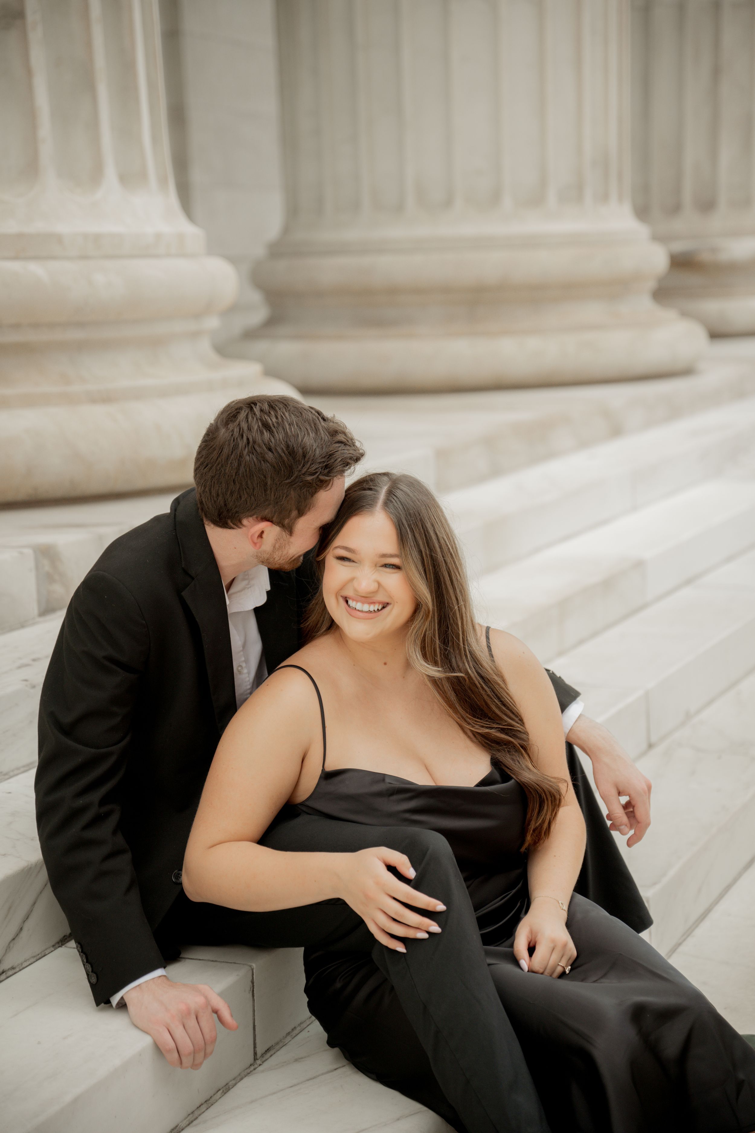 A couple embraces on a hillside near a winding stream with mountains in the background during golden hour.